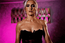 a woman in a black corset is standing in front of a pink background .