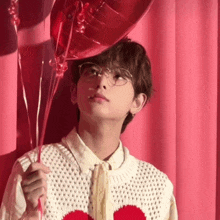 a young man wearing glasses is holding two red balloons .