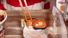 a person is holding chopsticks over a container of food on a table .