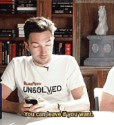 a man wearing a buzzfeed unsolved t-shirt looks at his phone