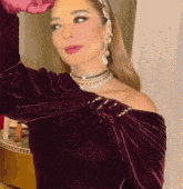 a woman wearing a purple velvet off the shoulder top with a necklace and earrings