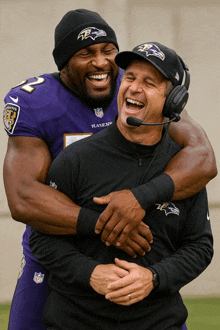 a man in a ravens jersey hugging another man in a black jacket