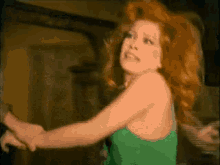 a woman with red hair is wearing a green tank top and has her arms outstretched .