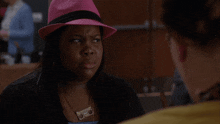 a woman wearing a pink hat and a cassette tape necklace looks at another woman