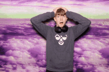 a man wearing headphones has his hands on his head in front of a purple sky