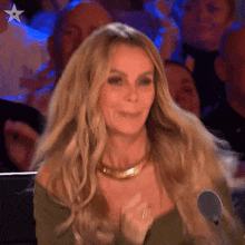 a woman with long blonde hair is sitting in front of a microphone and clapping her hands .