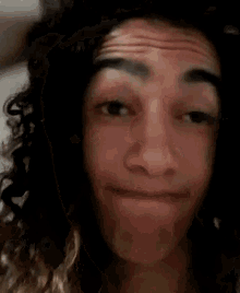 a young man with curly hair is making a funny face .
