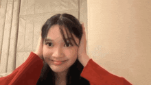 a woman in a red sweater is covering her ears with her hands and smiling .