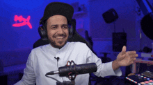 a man wearing headphones and a hat is smiling in front of a microphone with a red x on the wall behind him