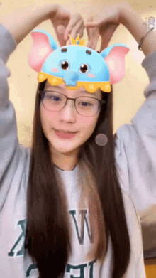 a woman wearing glasses and a dumbo mask makes a heart with her hands