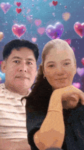 a man and a woman are posing for a picture with balloons in the shape of hearts behind them