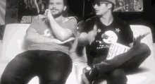 two men are sitting on a couch and one of them is holding a popcorn box .