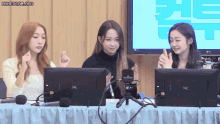 three girls are sitting at a table with monitors and microphones in front of a screen that says lg