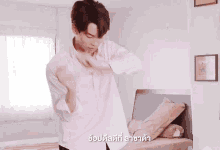 a man in a white shirt is standing in front of a bed in a room with foreign writing on the bottom
