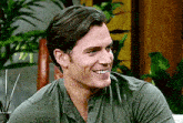 a man is smiling while sitting on a couch in front of a plant .