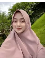 a woman wearing a pink hijab stands in front of a grassy hill
