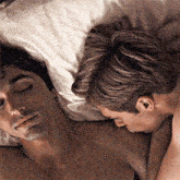 two men are laying on a bed with their eyes closed and one has his hand on the other 's chest .