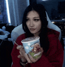 a woman in a red hoodie is holding a cup of ben & jerry 's ice cream .