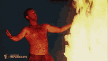 a shirtless man is standing in front of a fire with a knife .