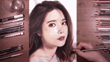 a drawing of a woman 's face is on a wooden table surrounded by colored pencils