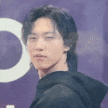 a man wearing a black hoodie is standing in front of a purple sign with a white letter c on it