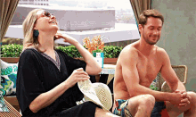 a shirtless man sits next to a woman who is sitting on a chair