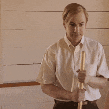 a man in a white shirt is holding a wooden stick in his right hand