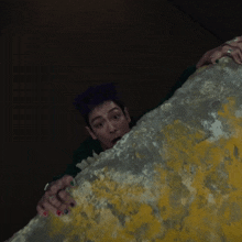 a man with purple hair and a green sweater with the letter m on the sleeve