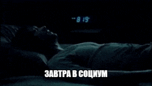 a man is laying in bed in the dark with the words `` завтра в социум '' written on the screen .
