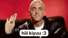a man is sitting on a couch with his hand up and a speech bubble .