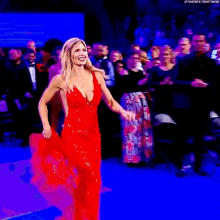 a woman in a red dress is walking on a red carpet in front of a crowd .