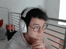 a man wearing headphones and glasses is sitting in front of a computer screen .