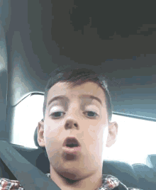 a young boy wearing a plaid shirt is sitting in the back seat of a car