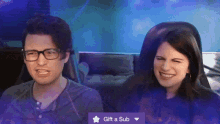 a man and a woman are sitting next to each other with a gift a sub button in front of them
