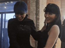 two women are standing next to each other in front of a brick wall and smiling