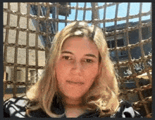 a woman with long blonde hair is sitting in front of a wicker fence