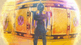 a man with his arms crossed is standing in front of a gold wall with a purple circle on it
