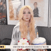 a woman with blonde hair is holding a cake with a candle on it in front of a poster that says mi