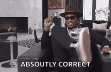 a man in a hat and sunglasses is sitting on a couch in a living room with his foot up .