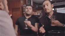 two men are standing next to each other holding glasses of wine and smoking cigarettes .