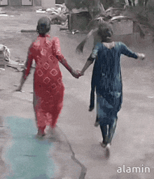two women are walking down a street holding hands and the word alamin is on the bottom left