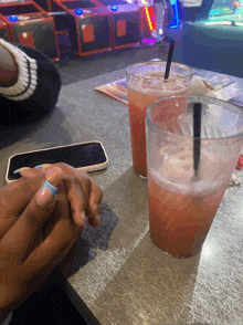 two glasses of pink liquid with straws on a table next to a phone