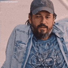 a man with a beard wearing a hat and a shirt that says ' ken mira ' on it