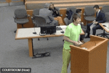 a man in a green shirt stands at a podium in a courtroom with the words courtroom ( host ) above him