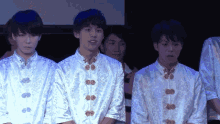 a group of young men are standing in a line wearing white shirts with gold buttons