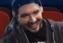 a man with a beard wearing headphones and a hat is smiling in a dark room