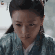 a woman wearing a blue kimono and earrings is looking down .