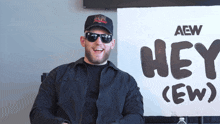 a man wearing sunglasses is smiling in front of a sign that says hey ( ew )