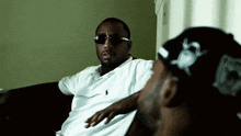 two men sitting on a couch one wearing sunglasses and the other wearing a hat with the letter r on it