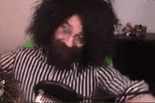 a man with long hair and a beard is wearing a striped shirt and glasses .